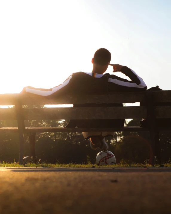 the person is sitting on a park bench in the evening sun