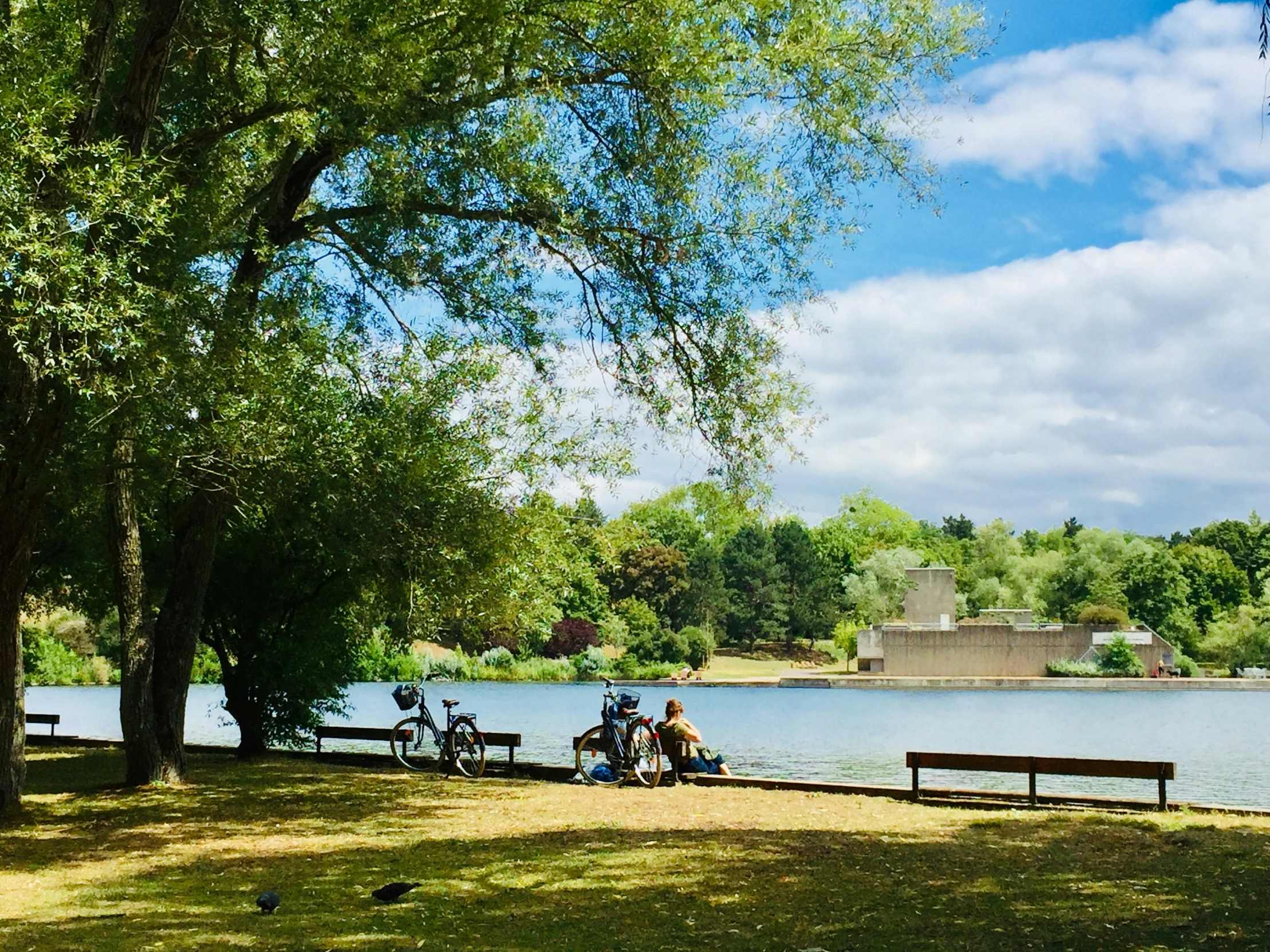 two people sit on benches next to a lake with their bikes nearby