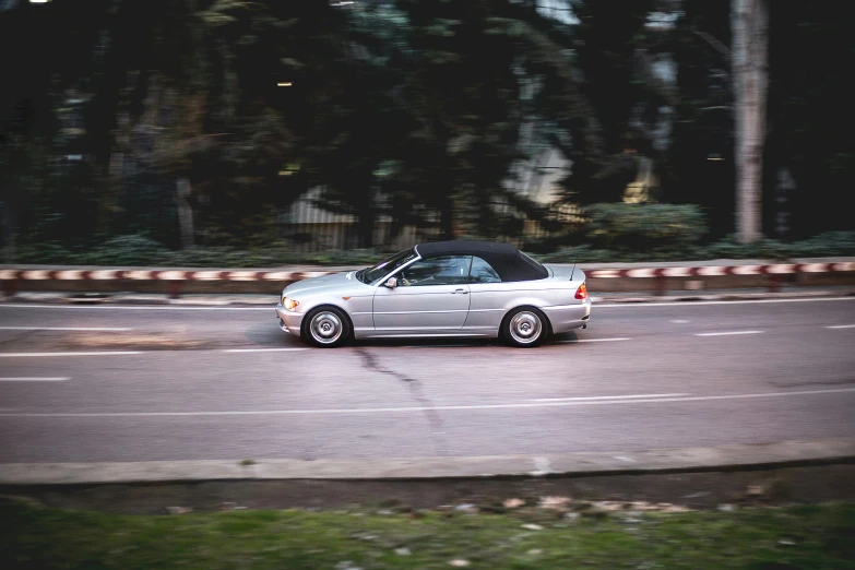 a silver sports car with black top driving down a road