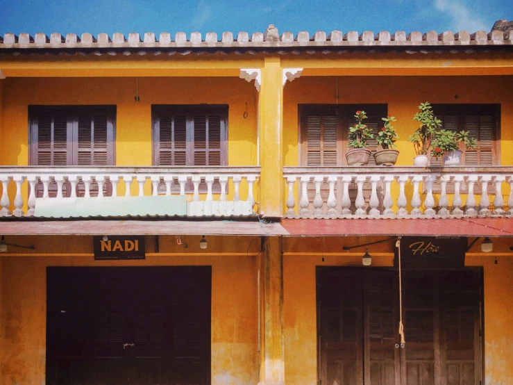 two tall yellow buildings with some pots full of plants