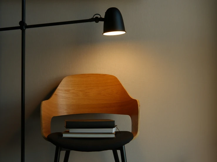 a lamp on a wall near a wooden chair and some books