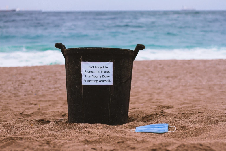 a trash can sitting in the sand on a beach