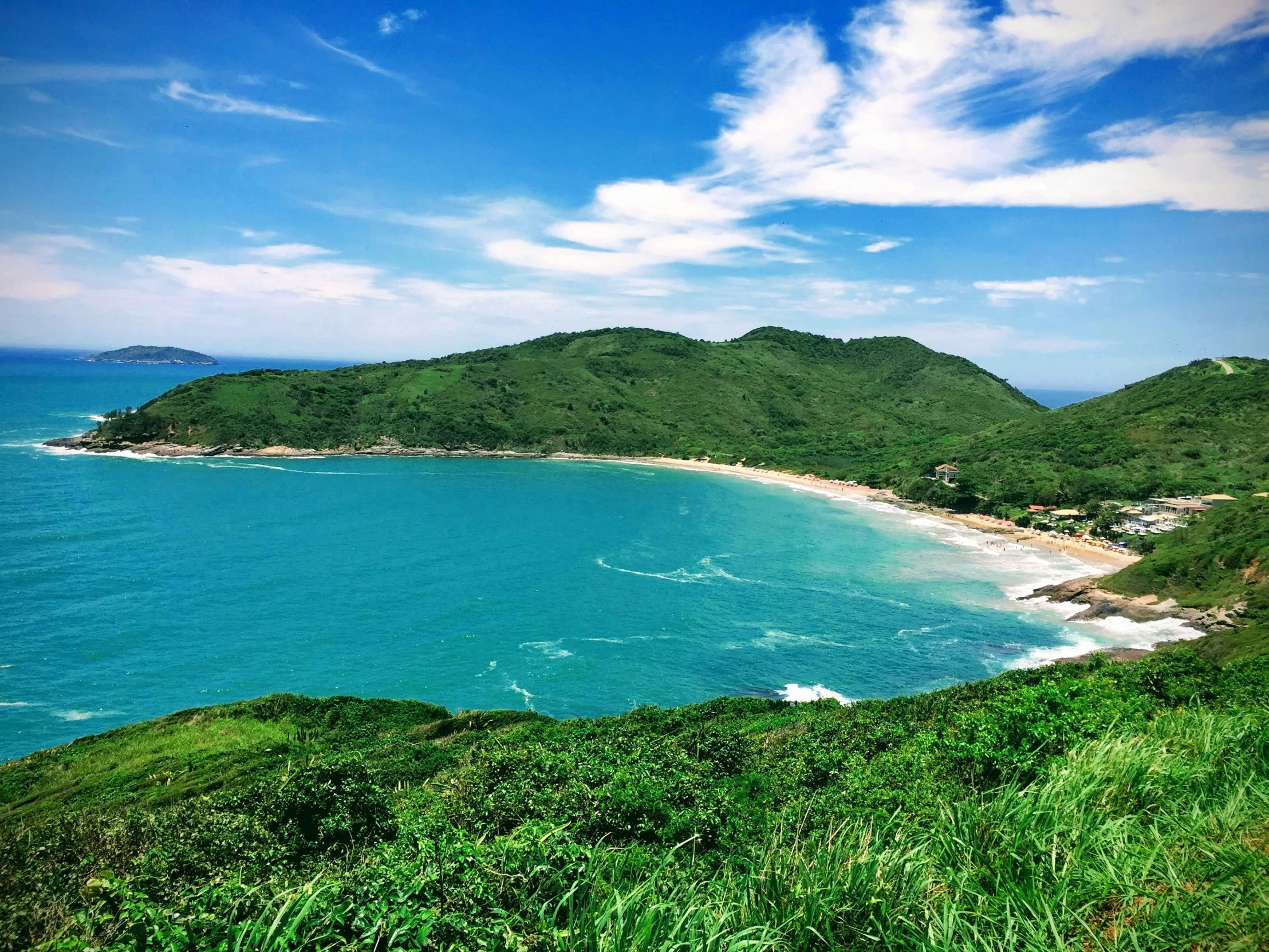 a sandy beach next to the ocean near a grassy hillside