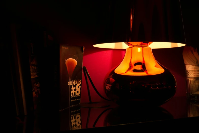 a lamp sits on a dark surface with a book on the side