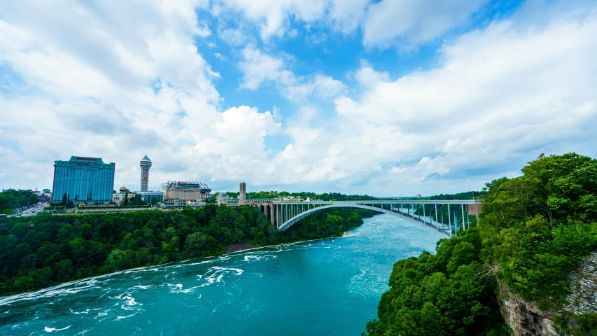 blue green waters and white clouds in the sky near a bridge