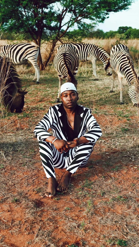 man with black and white outfit sitting near a herd of zes