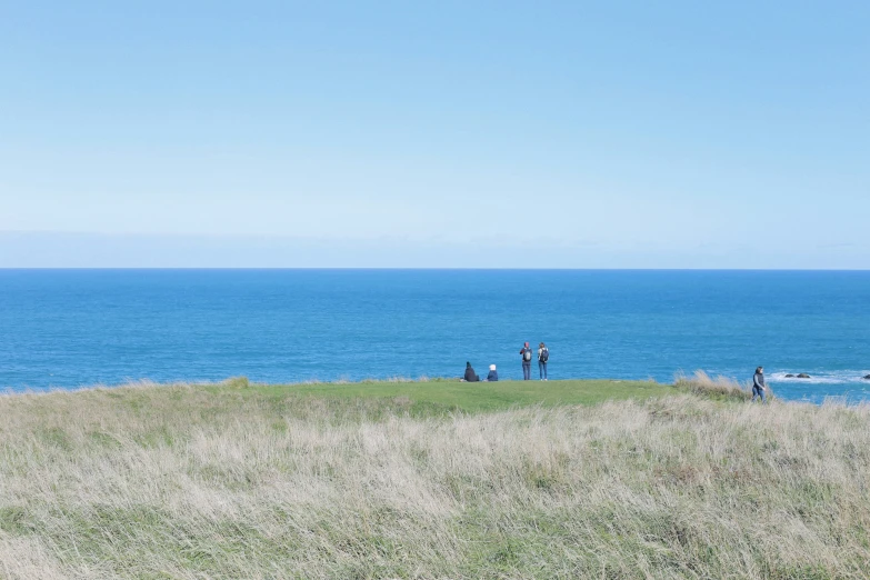 a group of people sit on a hill overlooking the ocean