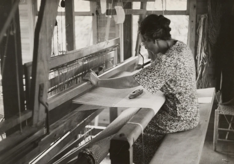 a woman is working with fabric on a large weaving machine