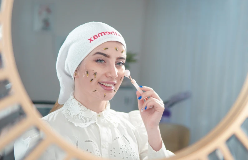 a woman putting on a gold face paint with a mirror