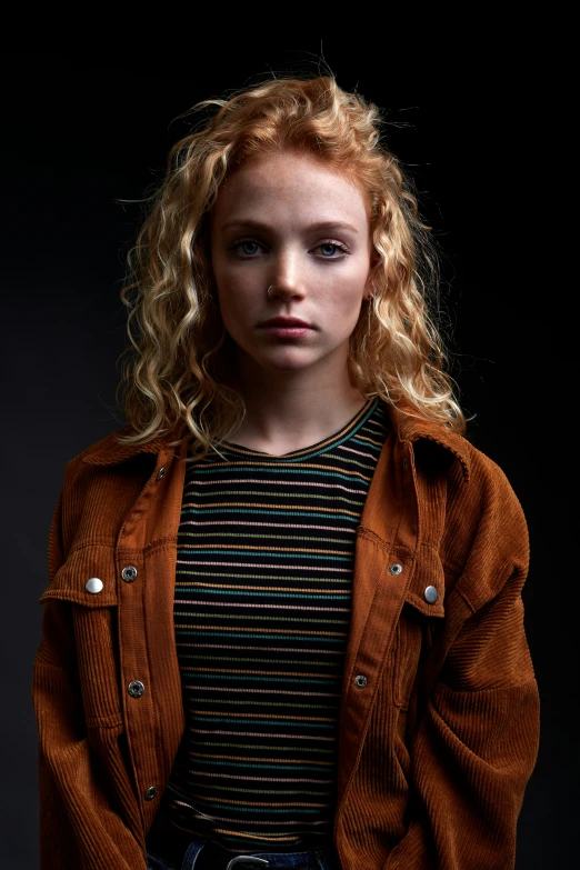 a young blonde girl with blue eyes and brown jacket