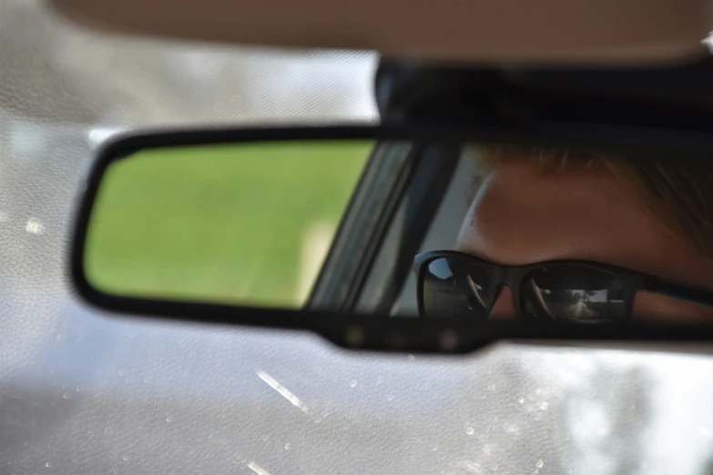 a man has his reflection in the mirror of his car