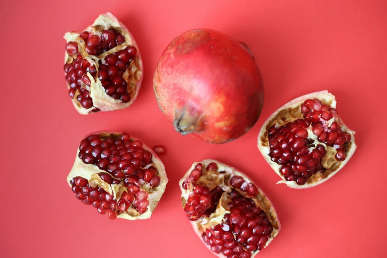 four pomegranates, an apple and a pear on a pink background