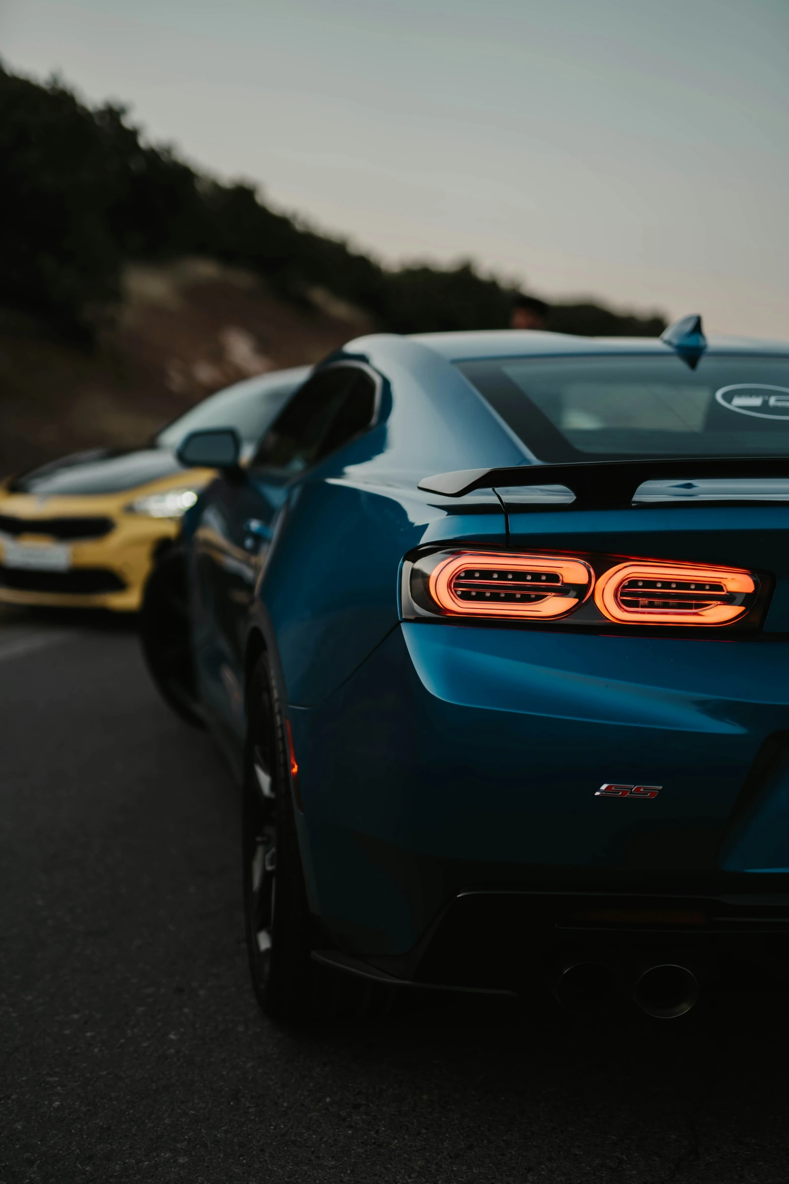 a blue car with lights turned on sits next to another one