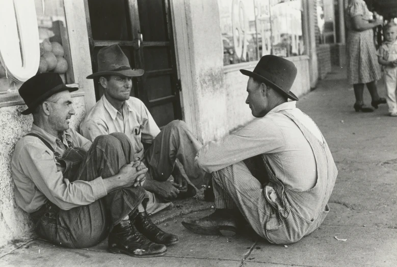 three men sitting on the ground talking to each other