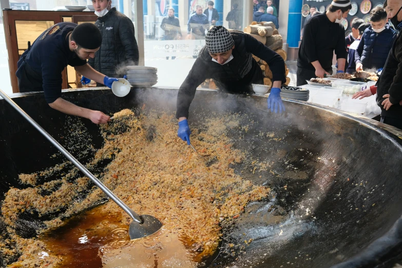 two men working in a large metal basin full of food