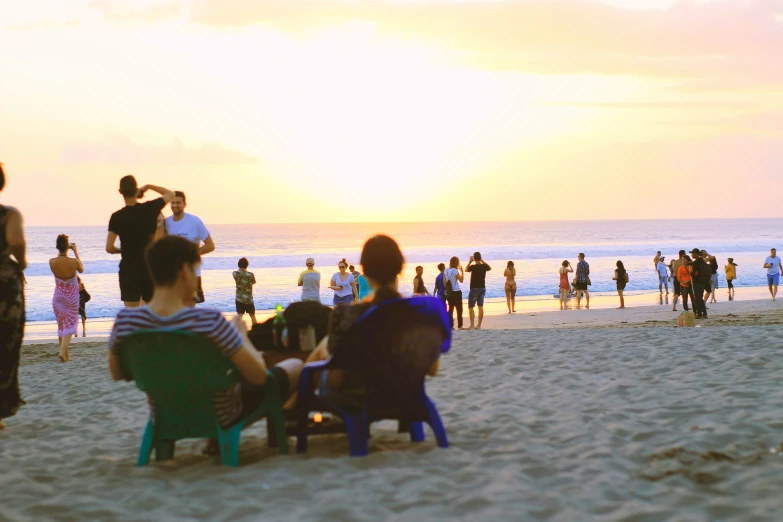 people stand on the beach as sun sets