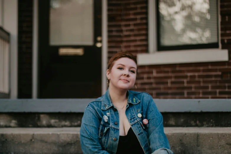 a woman sitting on steps wearing a jean jacket and black dress