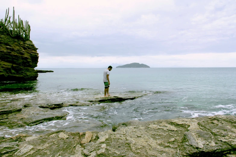 there is a male standing on the rocks of a cliff by the water