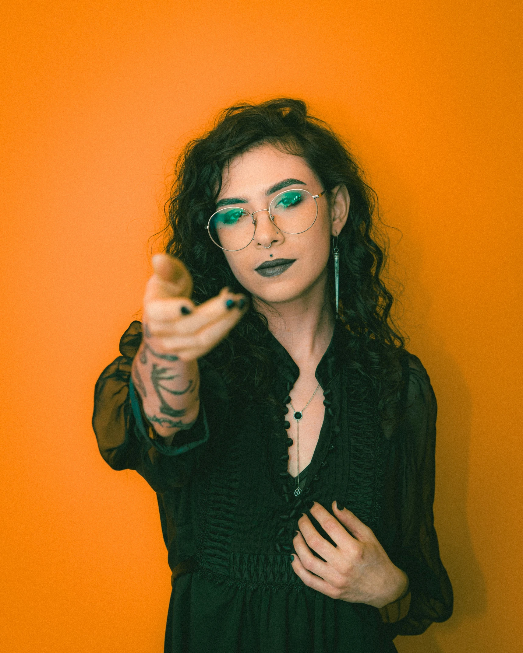 a woman points at the camera while wearing green glasses