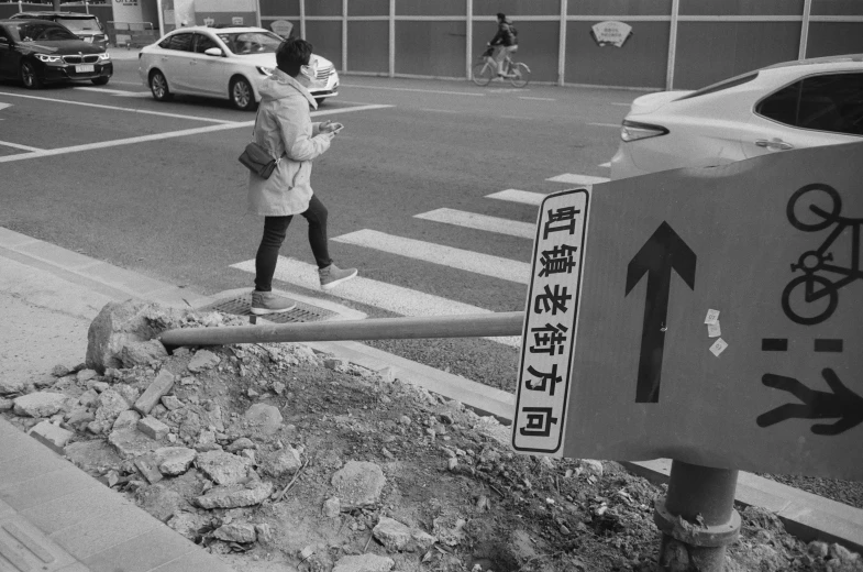 an asian woman walking on the street with a broken up sign in front