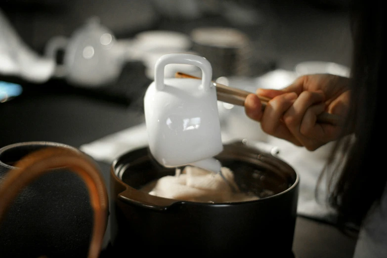 someone is using a container and a spoon to pour coffee into a mug