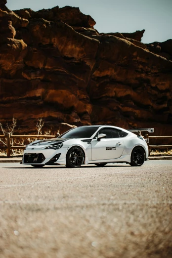 the sports car has black accents and is parked near some large rocks
