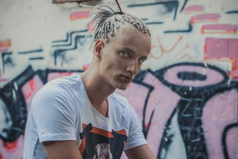 a man with some kind of hair in front of a graffiti wall