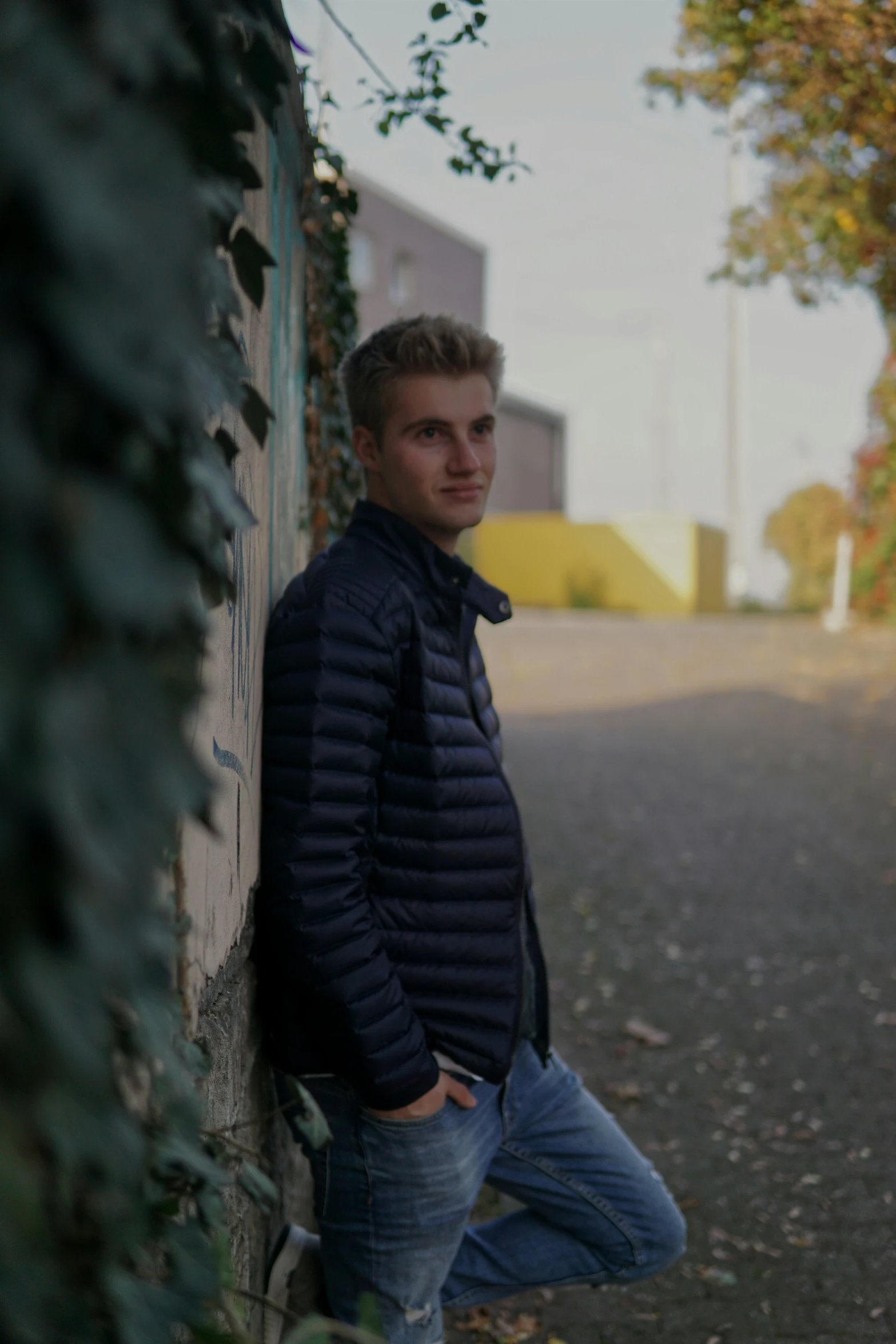 a young man standing next to a stone wall