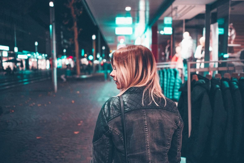 a woman in a black jacket standing on a city street at night