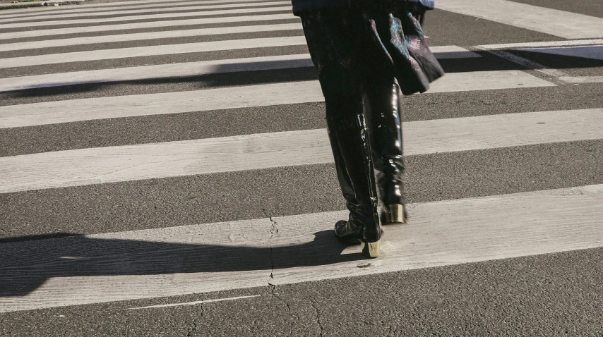 someone in black with leg high boots crossing the street