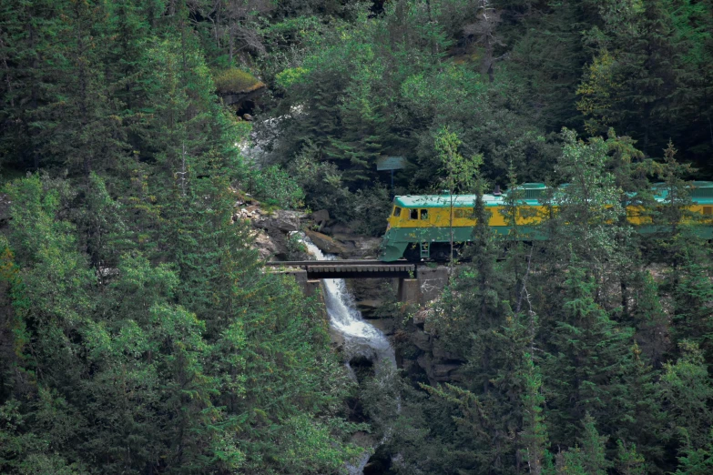 green and yellow train on a bridge over a waterfall