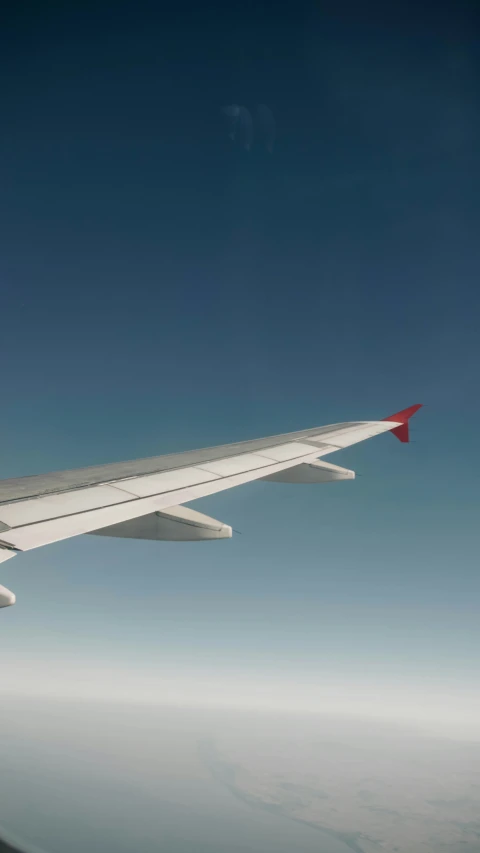 airplane wing and a cloudless sky with the bright red tip of the tail