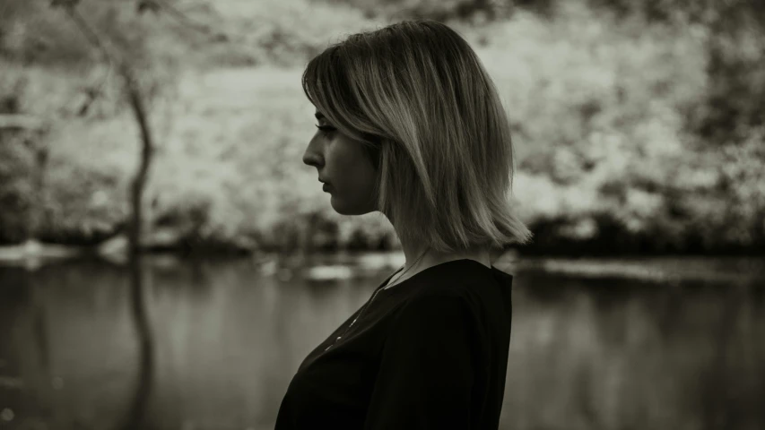 a woman with shoulder length blonde hair standing next to a lake