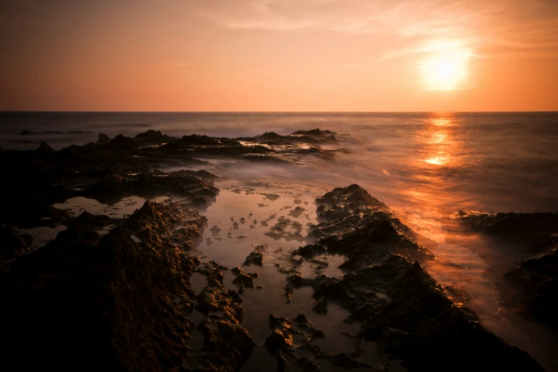 a rocky coastline at sunset with the sun shining down