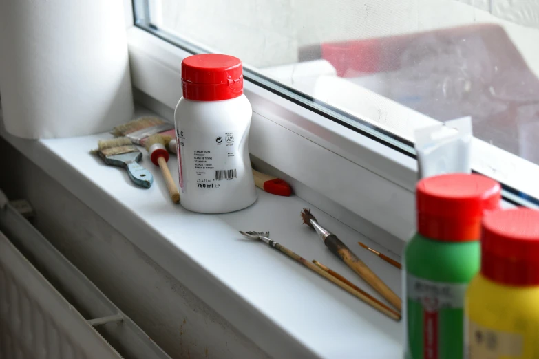a window sill with some paint and various paintbrushes