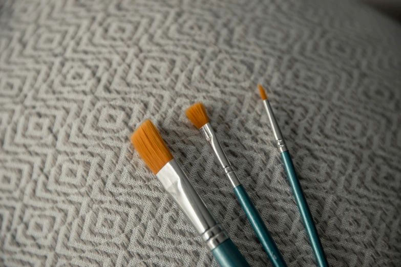 three paint brushes sitting on a piece of grey fabric