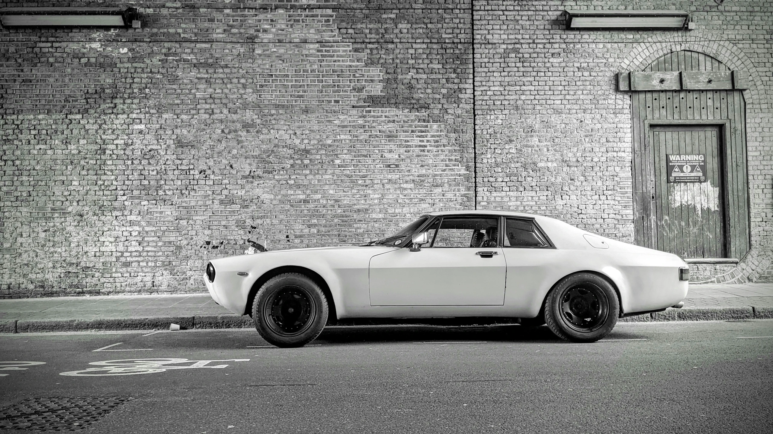 an old, white car parked in front of a brick wall