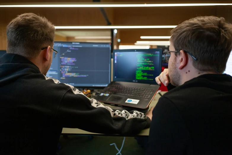 two men looking at a laptop screen with code on it