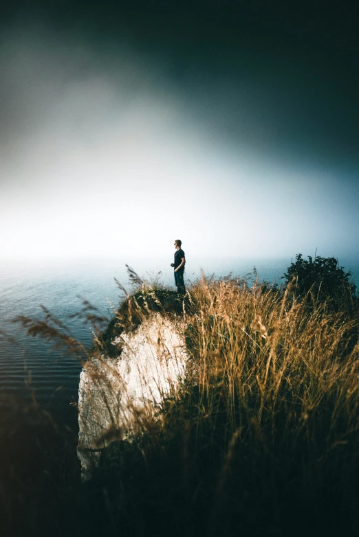 man on top of cliff overlooking ocean under storm clouds