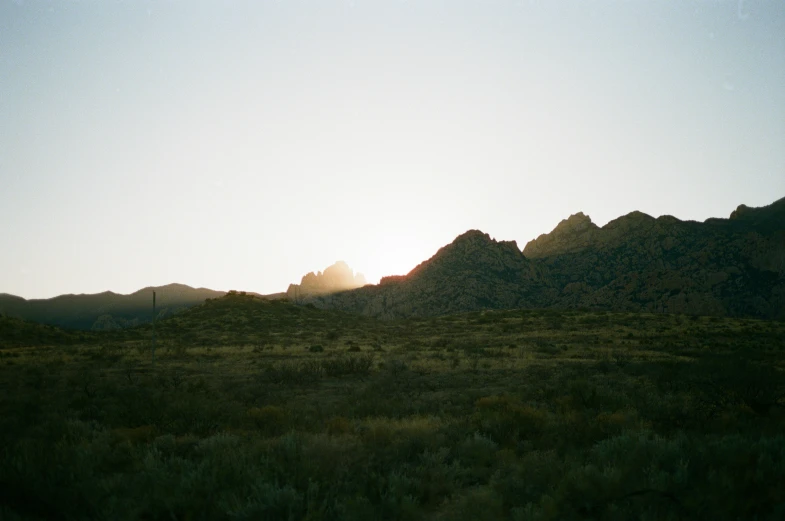 a bright sun rises over the mountains as seen from an empty field