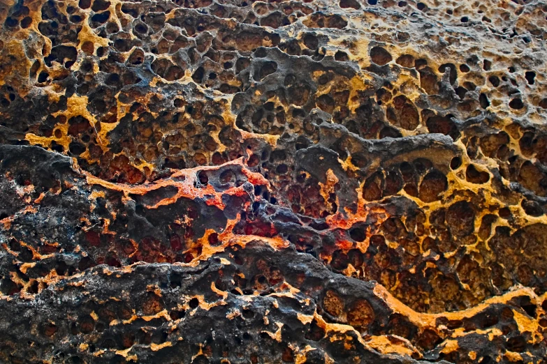 an abstract, textured rock formation with yellow, orange and blue spots