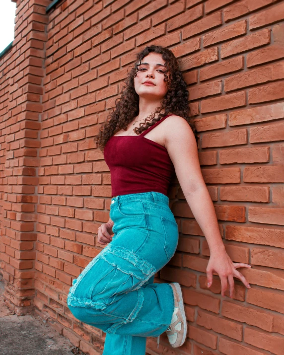 a young woman in jeans leaning on a brick wall