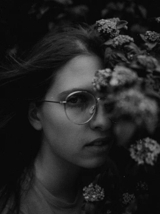 a woman in glasses surrounded by flowers and leaves