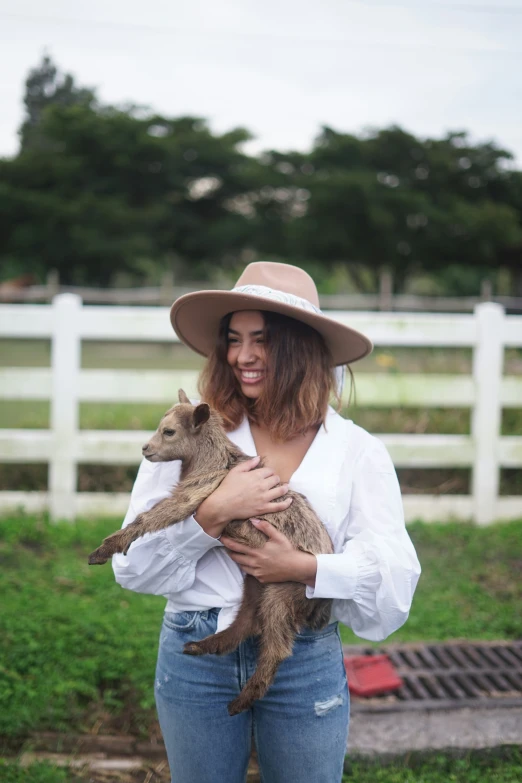 a woman holding a brown baby goat in a field