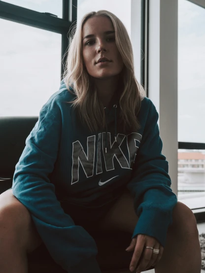 a person sits in front of a window, wearing a nike sweatshirt