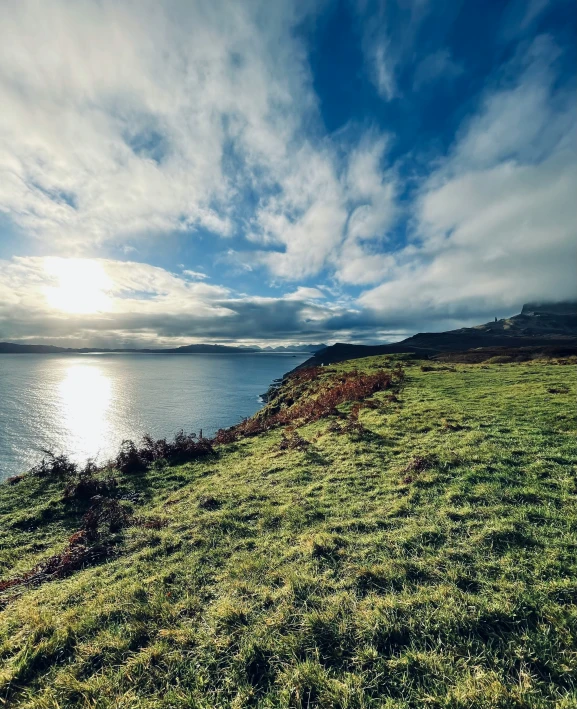 a blue sky and some clouds above a grassy hill by water