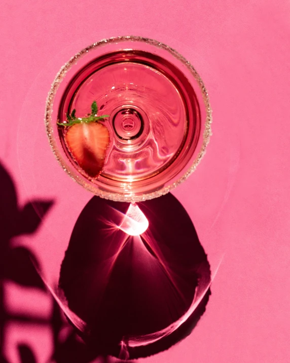 strawberries inside the clear cup of liquid in front of pink background