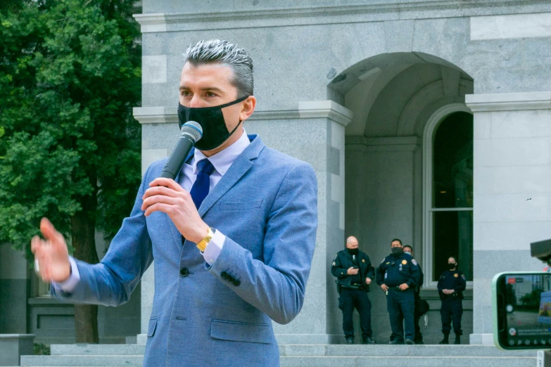 a man wearing a face mask and holding a microphone in front of a courthouse