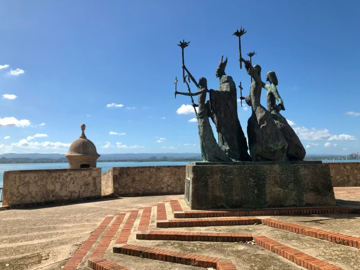 a large statue of four people holding hands next to a stone wall