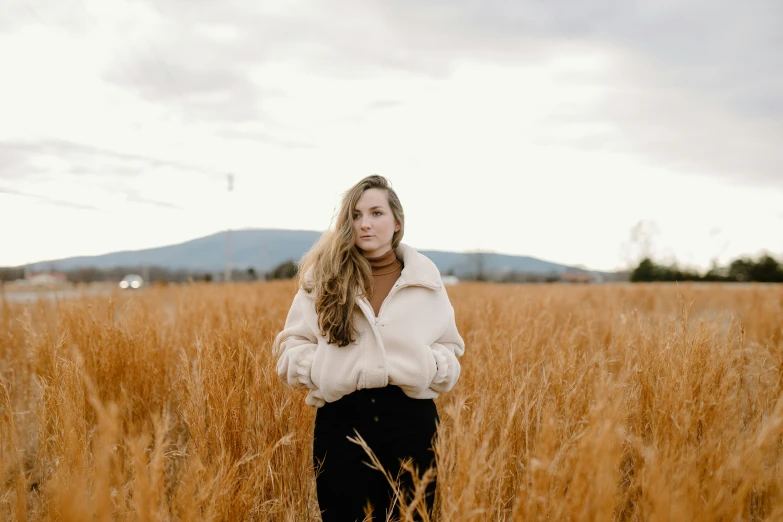 a woman standing in an open field with her long blonde hair in a white top